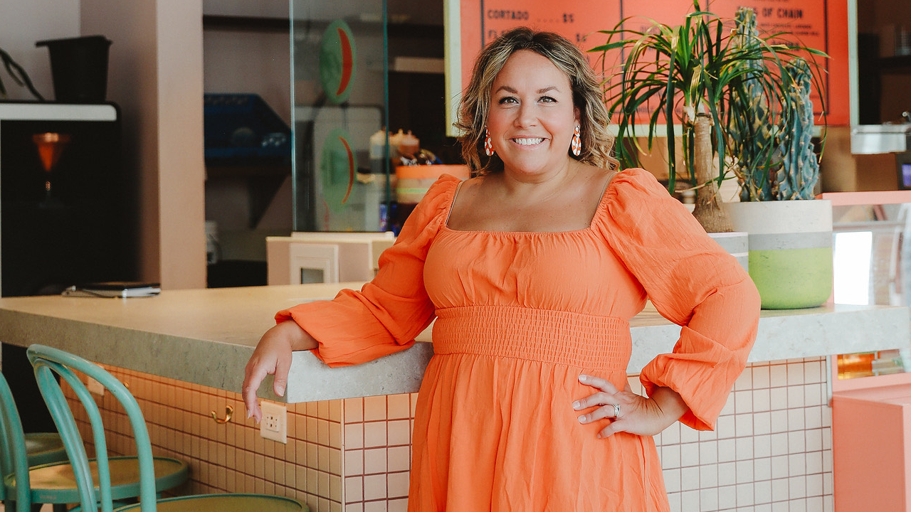 picture of a woman in an orange dress leaning on a counter smiling in a pose with her hand on her hip