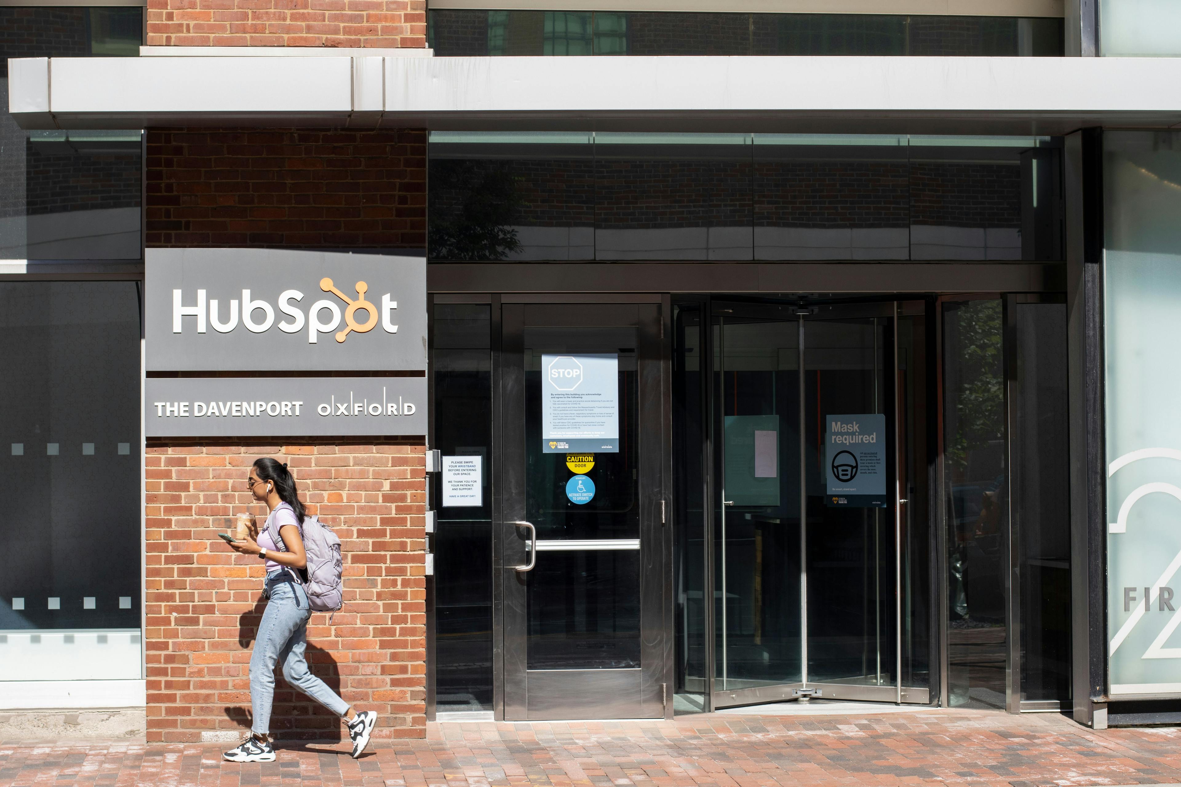 A woman with a backpack walking across the entrance to a Hubspot building.