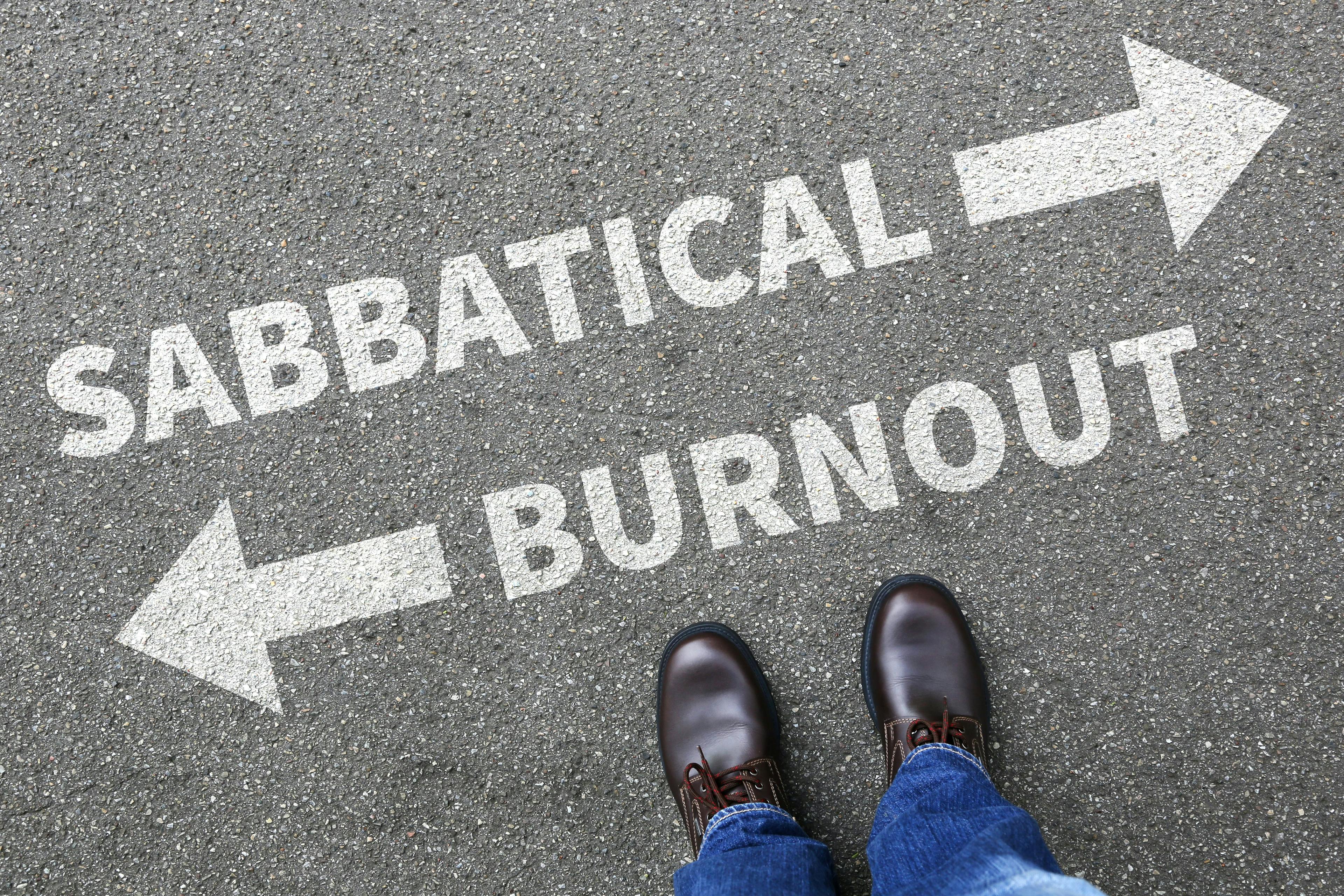 an image of the asphault with a white arrow pointing one way next to "sabbatical" and an arrow pointing the other way next to "burnout" and there's feet of a person in the bottom of the image